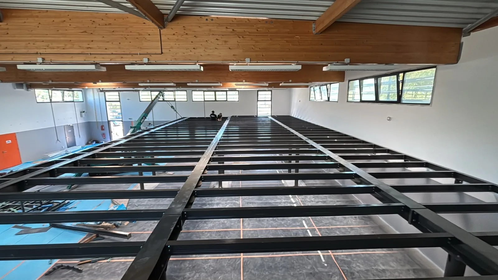 Ossature de mezzanine métallique noire en cours de montage dans un local professionnel, sous charpente bois